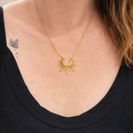 Gold necklace with a sunburst design worn by a person wearing black.