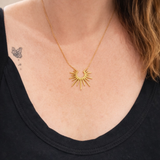 Gold necklace with a sunburst design worn by a person wearing black.