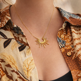 Gold necklace with a sunburst design worn by a woman in a patterned shirt.